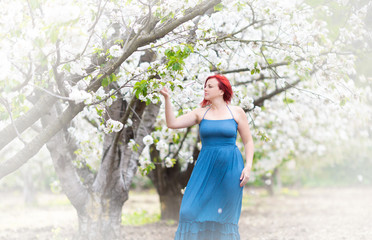 Waist up portrait of middle age Caucasian woman with red hair near white blossoming tree