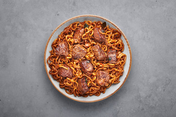 Ram-Don or Chapaguri noodles with beef steak in white bowl on grey concrete backdrop. Jjapaguri is a popular south korean dish with ramen and udon noodles and beef steak. Copy Space