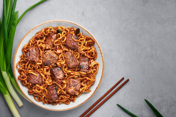 Ram-Don or Chapaguri noodles with beef steak in white bowl on grey concrete backdrop. Jjapaguri is a popular south korean dish with ramen and udon noodles and beef steak. Copy Space
