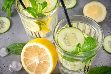 glasses of lemonade with yellow lemon, slices of fresh cucumber and mint on a gray