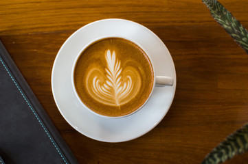 Latte art coffee in a white cup on a wooden table with books and leaves