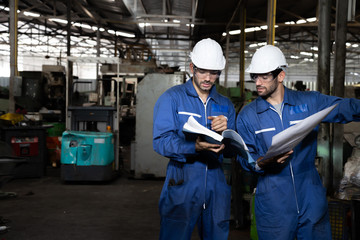 Factory engineer reading manual of machine operation and standing with blue working suite dress and safety helmet. Technical specialist  mechanics at heavy industry factory concept