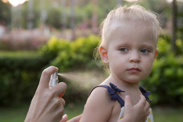 Mother applying mosquito and bugs repellent spray on her toddler girl.