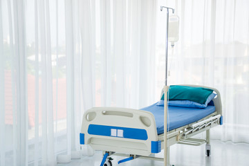 An empty hospital bed for sick patient with fluid bag and pole at a patient room or ward or an...