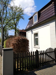 Holzzaun mit Türchen am Eingang zu einem stilvollen Wohnhaus im Frühling bei Sonnenschein in...