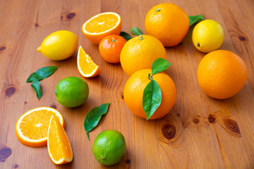 Vitamin citrus fruits oranges with leaves on wooden desk. Fresh mandarins, limes, lemons and sliced oranges laying on table. Top view. Studio shot. Nutrition and vegetarian concept