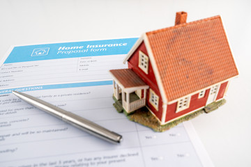Home insurance proposal form with miniature red house and pen laying on white office desk. Business, security and home concept.