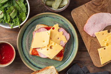 Sandwich with ham, cheese and fresh vegetables on wooden background.