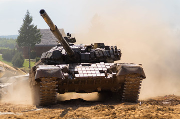 A tank drives through a village, raising clouds of smoke and dust around itself