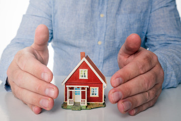 Business man with blue shirt are holding hands over red miniature house to illustrate the importance of insurance and security.