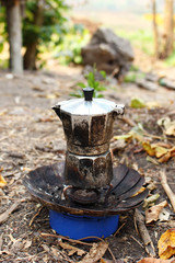 Geyser coffee maker with fresh hot coffee on portable gas burner on a campsite.