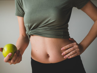 Beautiful sporty woman holds a green apple in hand near waistline. Healthy food
