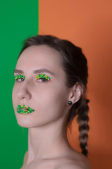 Young woman portrait with a candy makeup - multicoloured pastry topping pearls on her lips and eyelids. On a green and orange background. Easter theme.