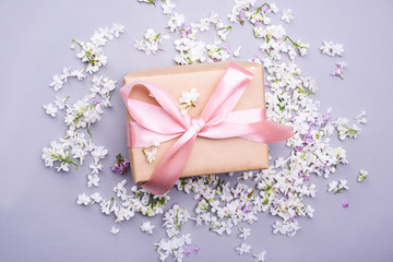Obraz na płótnie Canvas A beautiful gift with a satin ribbon against the background of lilac flowers.