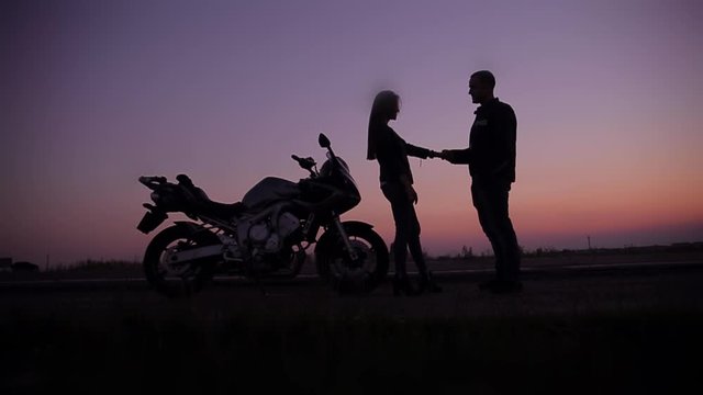 silhouette of a young couple of bikers meeting together on the road, landscape sky background motorcycle, bike, attractive girl coming to boyfriend. hipster at sunset. 
summer evening in nature