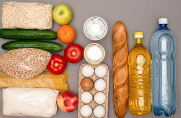 A set of products for delivery. Eggs, bread, sugar, groats, canned goods, tomatoes, apples, water, spaghetti on a gray background