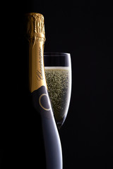 Champagne bottle and full glass with clear bubbles moody black background, high-end concept for luxury clamorous celebration, curves, silhouette, bottle shape close up. 