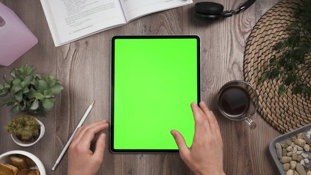 Big tab with chroma key green screen on it lay on the workplace table. Hand swipe left on touchscreen. Big screen of the tablet. Right hand swiping left. Work table with many things on it. Day time