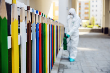 Man in sterile uniform and mask sterilizing fence of kindergarten from covid-19 / corona virus.