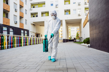 Full length of man in sterile uniform and mask sterilizing surface outdoors from corona virus, fungus and disease.