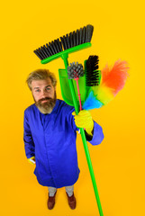 House cleaning. Housekeeping. Bearded man in uniform with cleaning equipment. Professional cleaning. Clean up. Cleaning tools. Broom. Dust brush. Household. Full height.