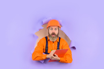 Through paper. Advertising. Repair. Building concept. Engineer making notes. Surprised repairman with folder. Construction worker with folder. Repairman with folder. Man in hard hat. Helmet.