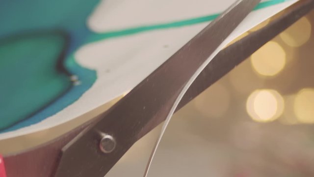 Close up of scissors cutting paper with defocused fairy lights in background. 4K resolution macro shot. Shallow depth of field. High quality audio recorded with condenser microphone.
