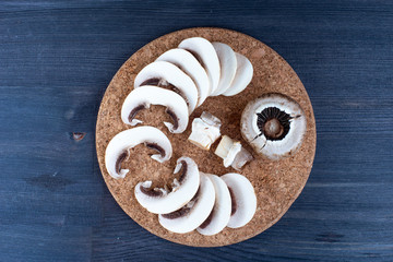 White sliced champignons on a round plate, on wooden table. Mushrooms on wooden background.