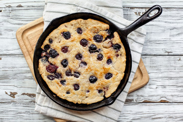 Fresh made homemade cherry cobbler baked in a cast iron pan over a rustic white wood table. Image shot from top view.