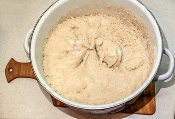 Fototapeta na wymiar raw dough in an enamel pan, yeast dough in a white pan on the tabl