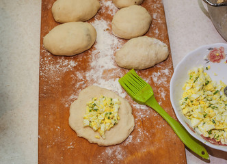 filling for pies on a wooden board,
pie filling green onion and egg,
filling for pies on homemade dough,
silicone brush on a wooden board,raw homemade stuffed yeast pastry pies