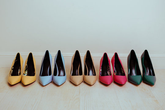 Multiple pairs of kitten, stiletto high heels of different colors. Woman classic dress shoes aligned on a floor.