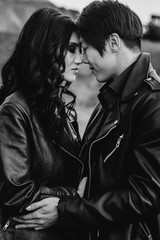 An Asian couple in love in black leather clothes walk in nature among the trees. Black-white