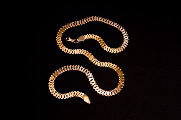  Gold necklace for men.  Long, wide chain, in a snake shape, isolated on a black background.