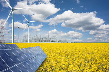 Renewable or green energy concept with wind turbines solar panels and yellow raps field on blue sky with clouds - 344260761