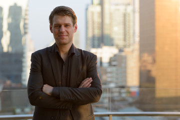 Young handsome businessman in suit with arms crossed against view of the city