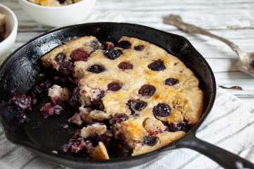 Half eaten fresh made homemade cherry cobbler baked in a cast iron pan over a rustic white wood...