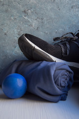 Fototapeta premium Black sneaker with white details and holes, a blue rolled towel and a blue foam rubber ball on a white base and a background in blue and gray tones.