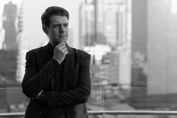 Young handsome businessman in suit thinking against view of the city in black and white