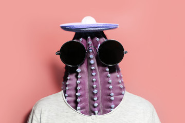 Minimal pop-art collage portrait of green cactus-headed man wearing black round shades and mexican hat on background of coral pink color.