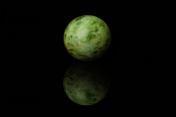 A malachite ball, similar to a planet, lies on a glossy black glass, in which it is visible