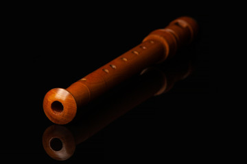 A wooden flute lies on a black glossy glass in which its reflection is visible