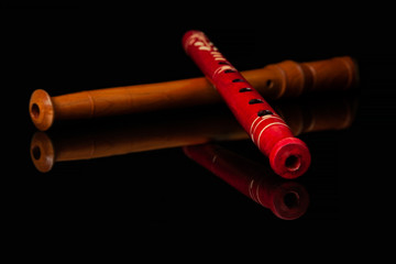Two wooden flutes lie on black glossy glass in which their reflection is visible