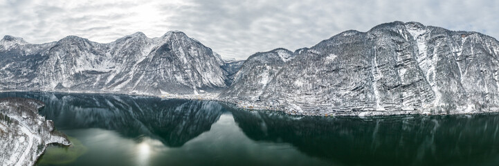 Aerial panoramic drone shot of Hallstatt village by lake surrounded by snow covered mountain in overcast winter time in Austria