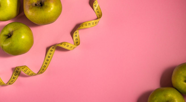 Weight control concept with green apples and measuring tape on the pink background. Lose weight and dieting idea. Layout design with copy space