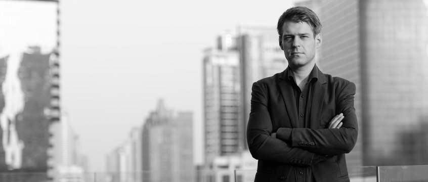 Young handsome businessman in suit with arms crossed against view of the city