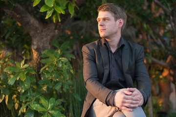 Young handsome businessman in suit sitting in nature outdoors