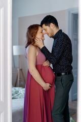 Naklejka premium Happy pregnant couple. Loving husband wants to kiss tenderly his pregnant wife touching her face at home