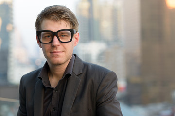 Face of young handsome nerd businessman with eyeglasses against view of the city