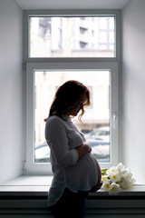 Portrait pretty pregnant lady with white tulips at home thinking about her motherhood